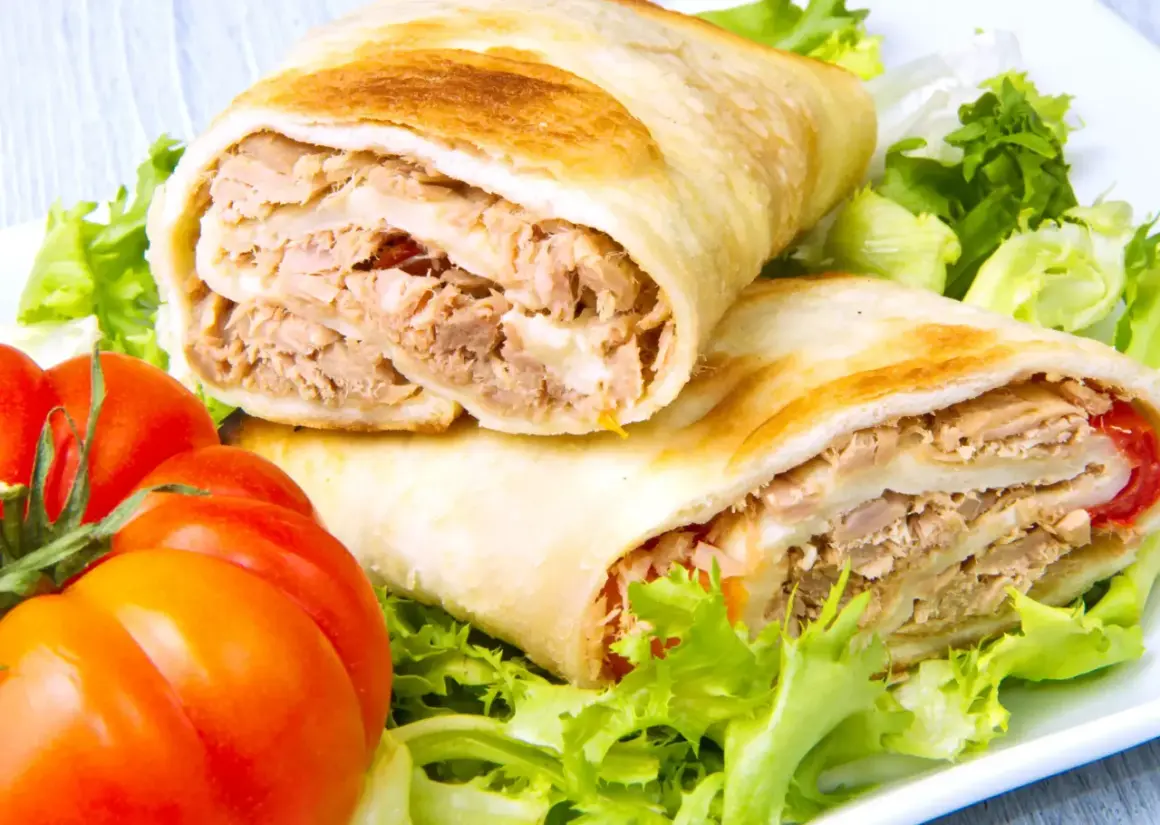 Dos rollos de wrap de atún, rellenos de atún desmenuzado y queso, servidos con lechuga fresca y tomates.
