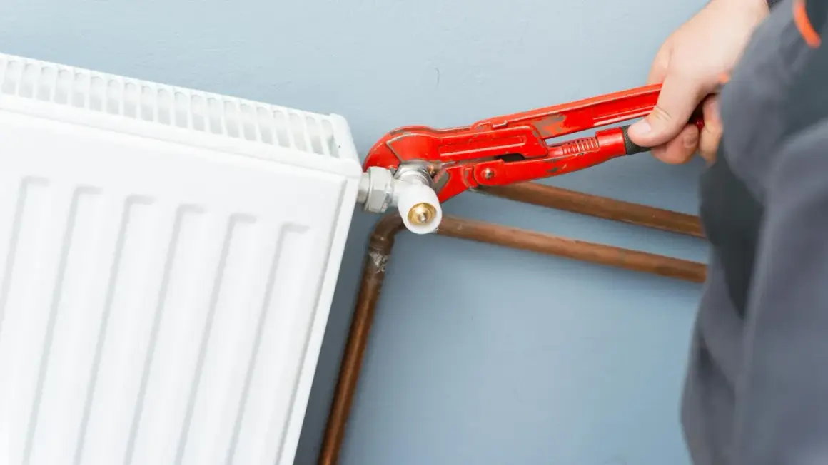 Mano con pinza rossa che lavora sulla valvola di un termosifone bianco, mostrando come smontare un termosifone.