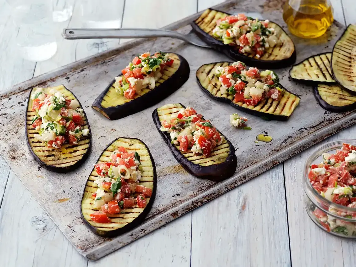 Grilla aubergine halvor toppade med en fräsch blandning av tomat, fetaost och örter. Perfekt som förrätt eller tillbehör.