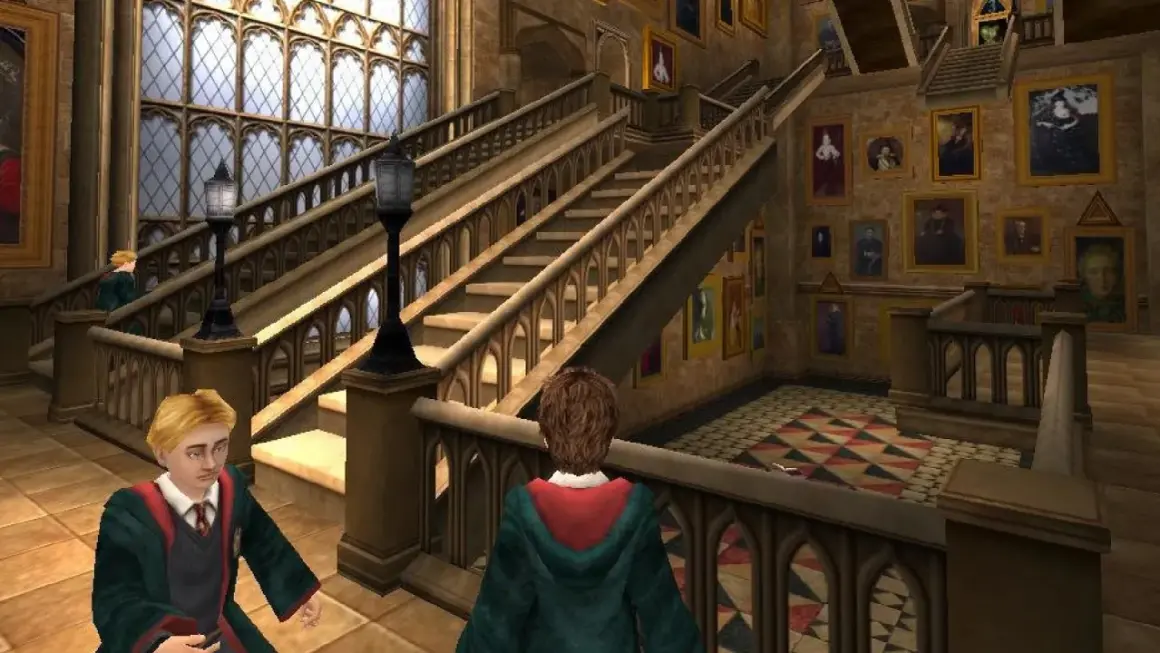 Dwóch uczniów w szatach Gryffindoru przemierza korytarz Hogwartu, jak w grach Harry Potter. Obok schodów wiszą ruchome portrety.