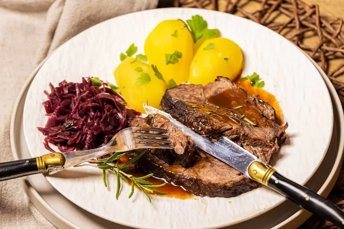 Zarter Rinderbraten im Ofen, serviert mit Salzkartoffeln und Rotkohl. Ein Messer und eine Gabel sind bereit, das saftige Fleisch anzuschneiden.