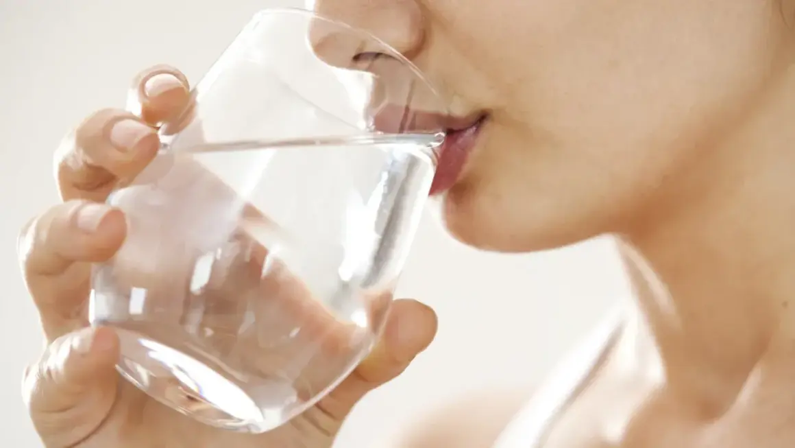 Une femme boit un verre d'eau. Une question importante pour les jeunes mamans : quelle eau boire allaitement ?