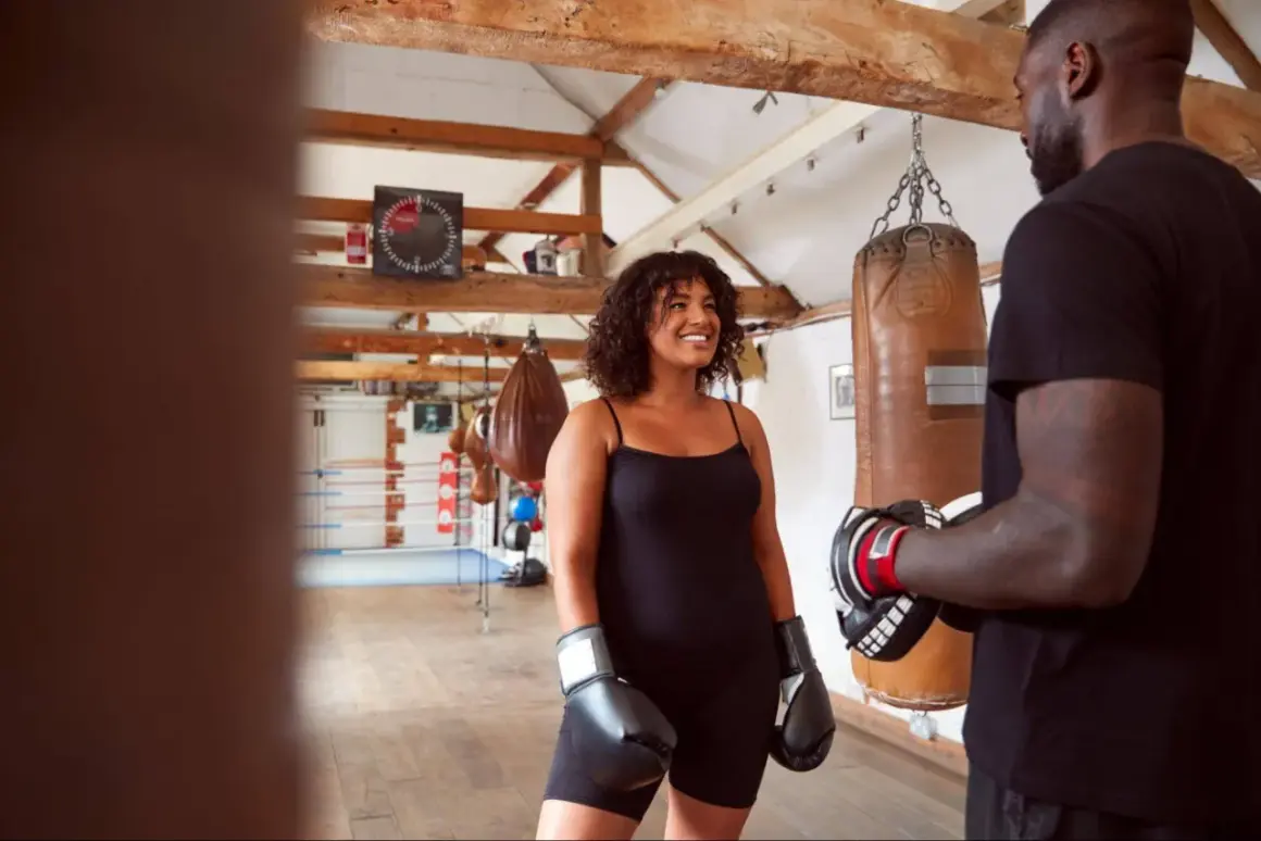 A woman in boxing gloves smiles at a trainer in a gym. This scene suggests that boxing makes you stronger, both physically and mentally.