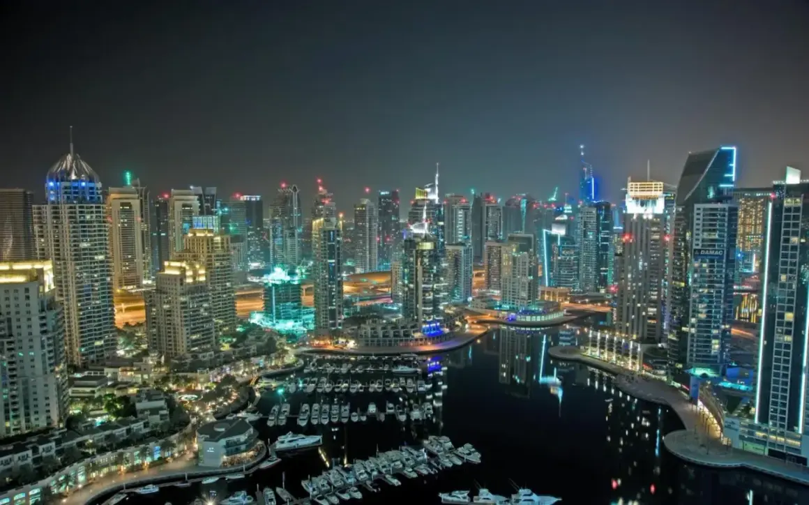 Widok nocą na drapacze chmur i przystań jachtową w Dubaju.