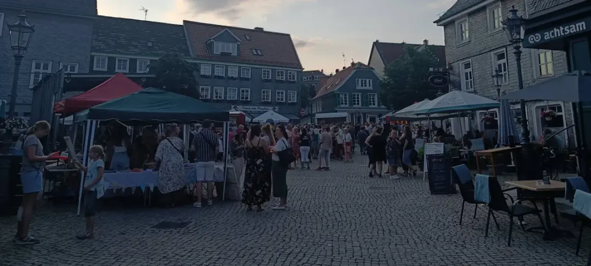 Menschen genießen den Abend auf dem Markt Remscheid. Stände mit Zelten und Tische unter Sonnenschirmen laden zum Verweilen ein.