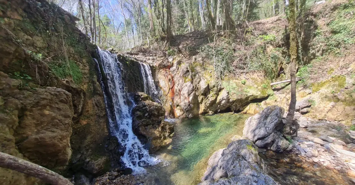 Cascata nella riserva naturale Alto Merse, con rocce colorate e acqua cristallina che forma una pozza verde smeraldo.