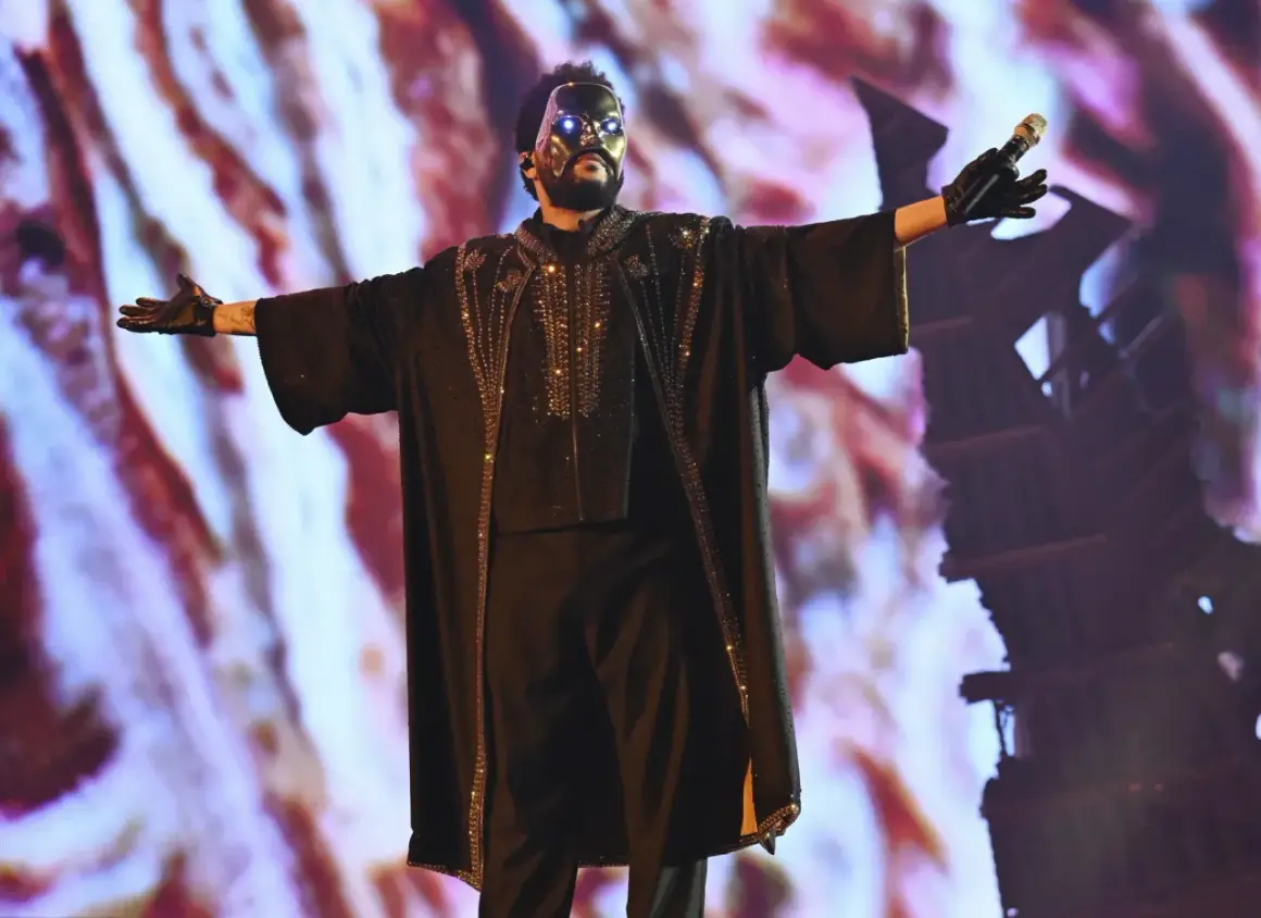 The Weeknd w czarnej, zdobionej masce i stroju, śpiewa na koncercie.