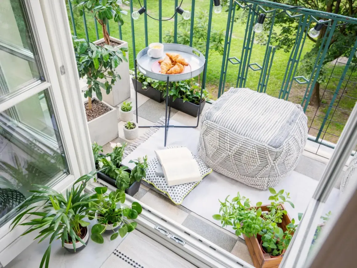 Gemütliche Balkon Ideen: Pflanzen, Kissen, Hocker und ein Tablett mit Croissants laden zum Verweilen ein.