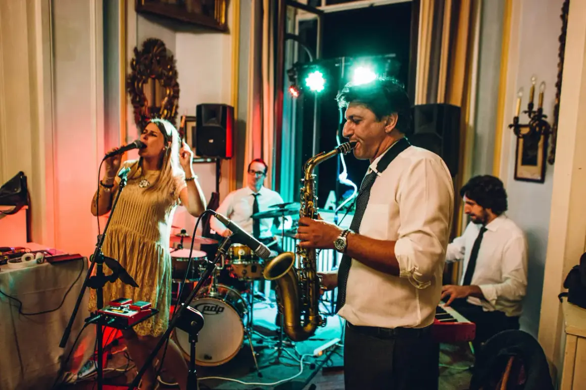 Una band suona musica dal vivo per un matrimonio. La cantante è in primo piano, mentre un sassofonista, un batterista e un tastierista completano il gruppo.