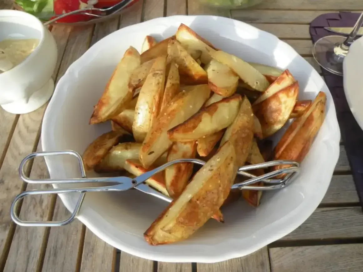En skål med gyllene klyftpotatis i ugn, redo att serveras med tång.