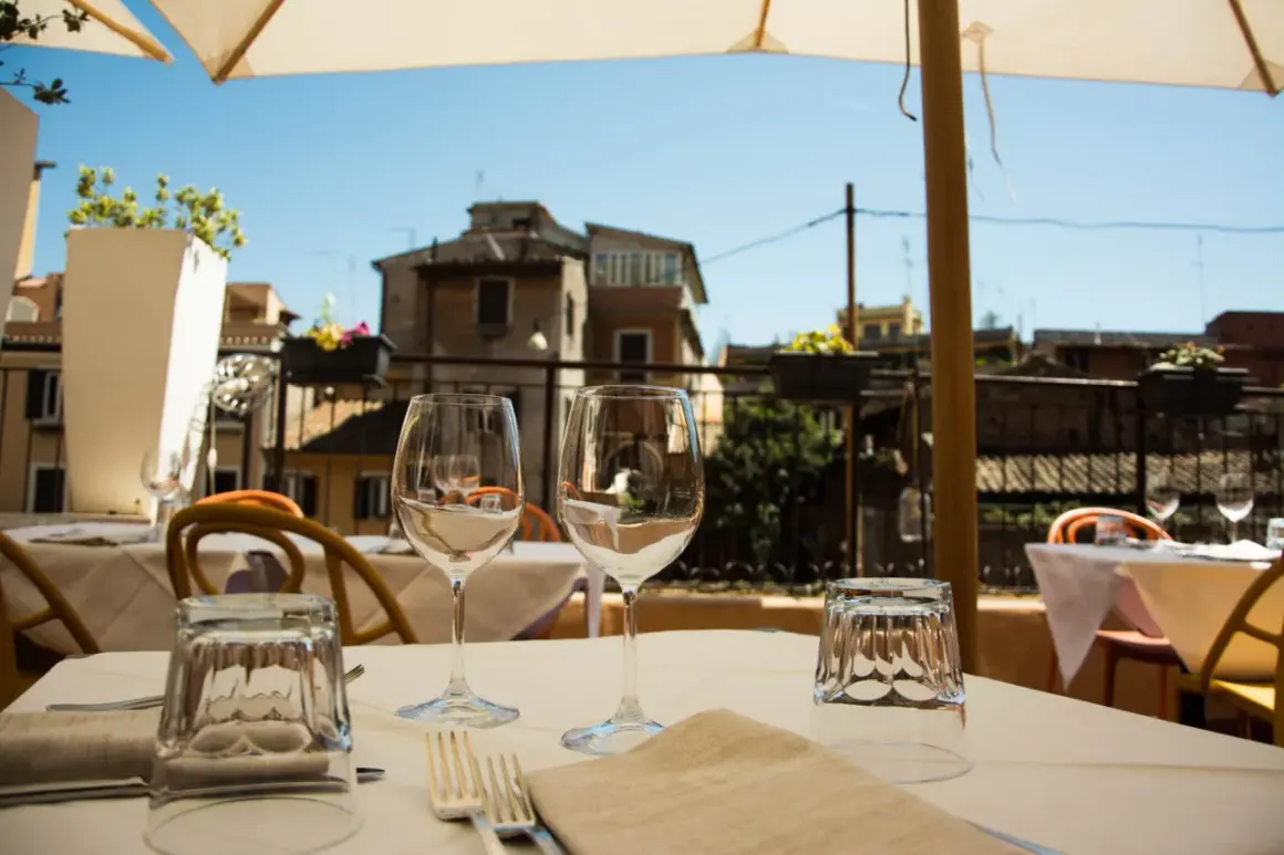 Tavola apparecchiata con bicchieri e posate in un ristorante all'aperto, con vista sui tetti di Roma. Un'atmosfera perfetta per scoprire i migliori ristoranti di Roma.