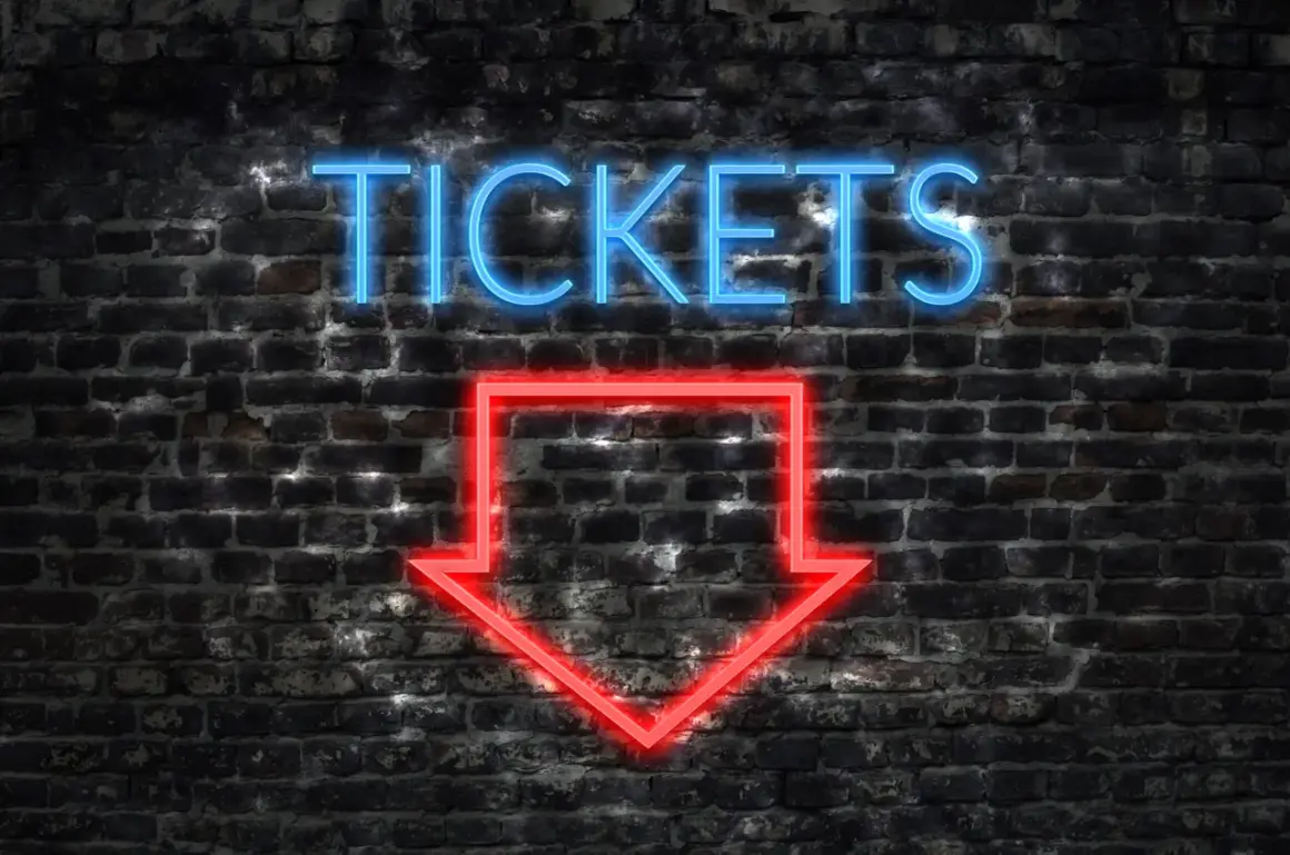 Napis "TICKETS" neonem w kolorze niebieskim i czerwona strzałka w dół na ceglanej ścianie.