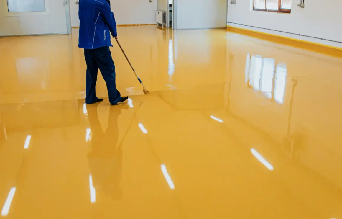Operaio stende resina poliuretanica o epossidica gialla su un pavimento lucido, creando un ambiente moderno e resistente.