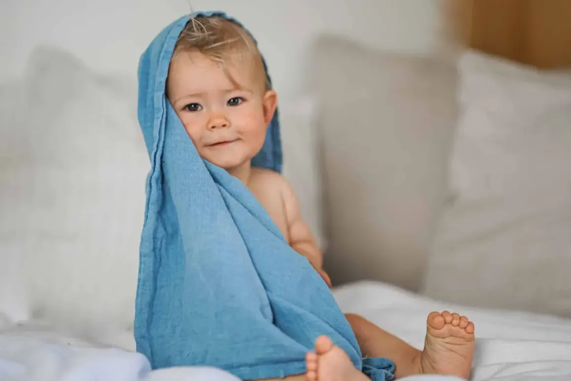 Ein süßes Baby von 12 Monaten, eingewickelt in ein blaues Tuch, schaut neugierig in die Kamera.