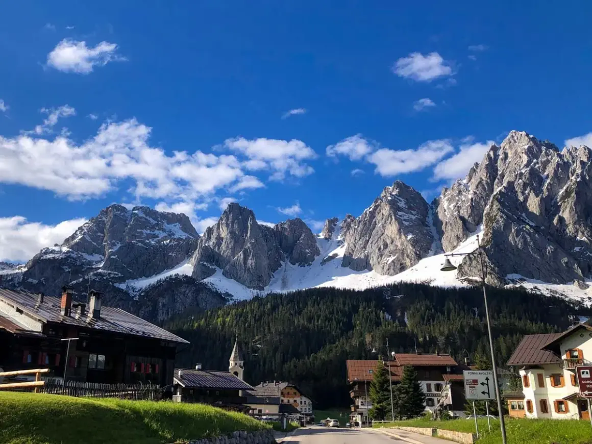 Villaggio alpino con case in legno e montagne innevate sullo sfondo. Un assaggio di cosa vedere in Carnia, tra natura e tradizione.