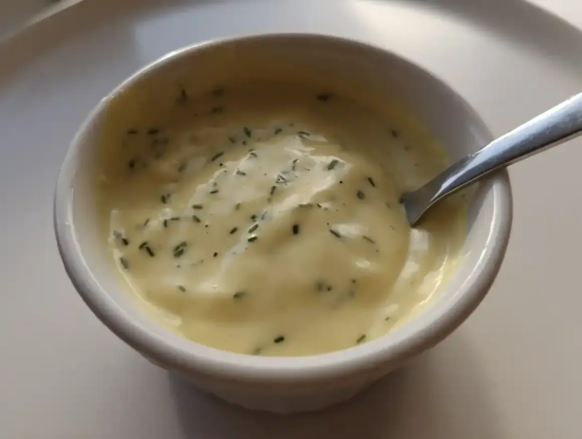 En skål med krämig, gul vegansk bearnaisesås med finhackade örter. Perfekt för ditt veganska bearnaisesås recept.