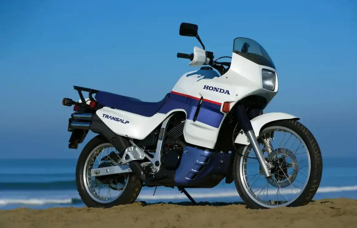 Biało-niebieski motocykl Honda Transalp 650 stoi na plaży.