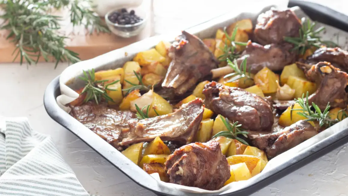 Agnello al forno marinato con patate e rosmarino, un piatto succulento e profumato, pronto per essere gustato.