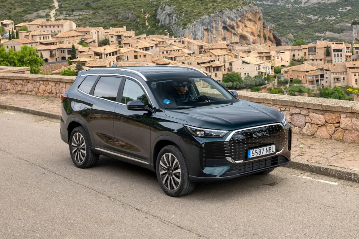 Ebro S800 PHEV, un SUV moderno, aparcado en una carretera con un pueblo pintoresco de fondo.