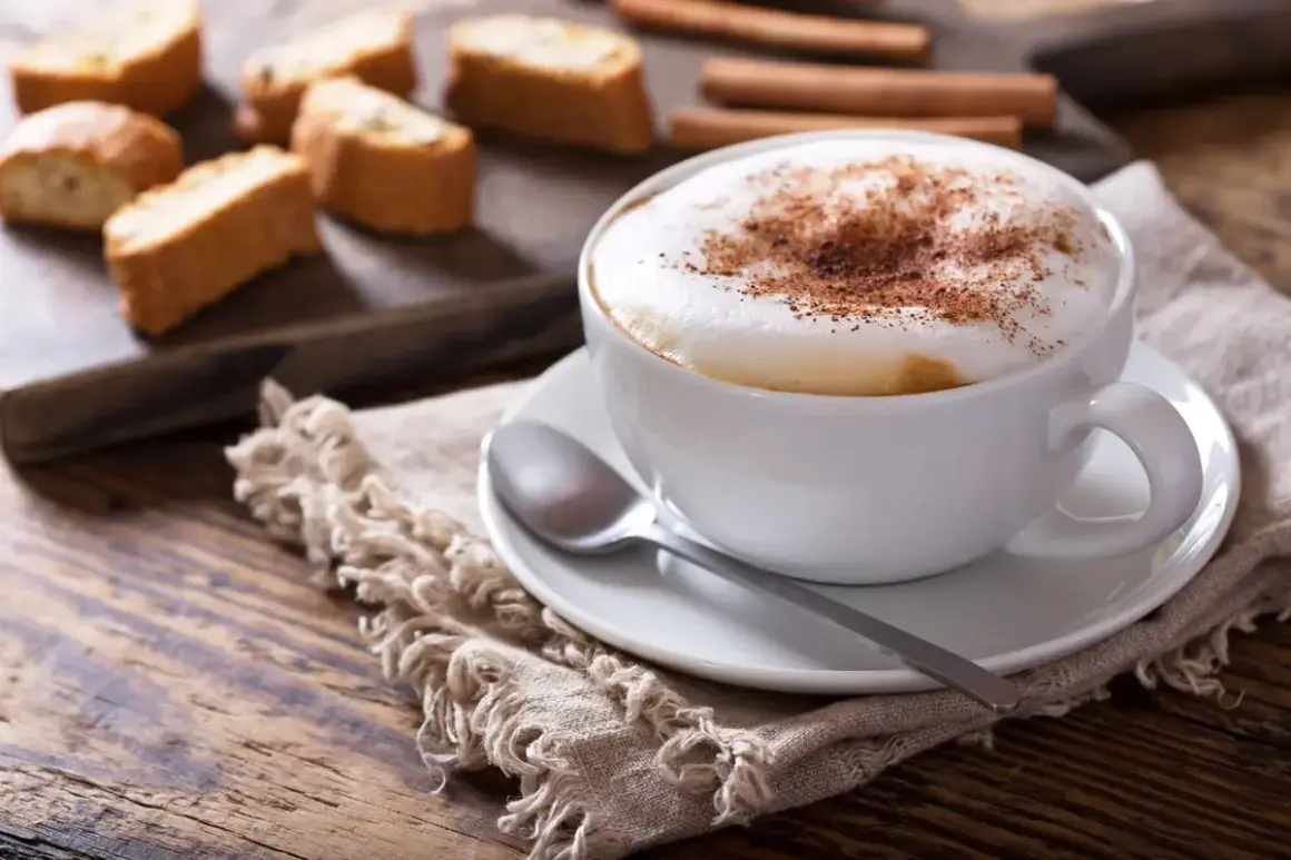Un cappuccino senza latte, con schiuma soffice e cacao, accompagnato da biscotti secchi e cannella su un tavolo di legno rustico.