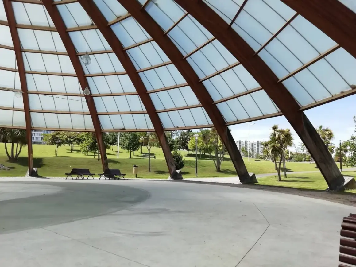 Estructura de madera y cristal en el parque de Eiris, con vistas a césped, árboles y edificios.