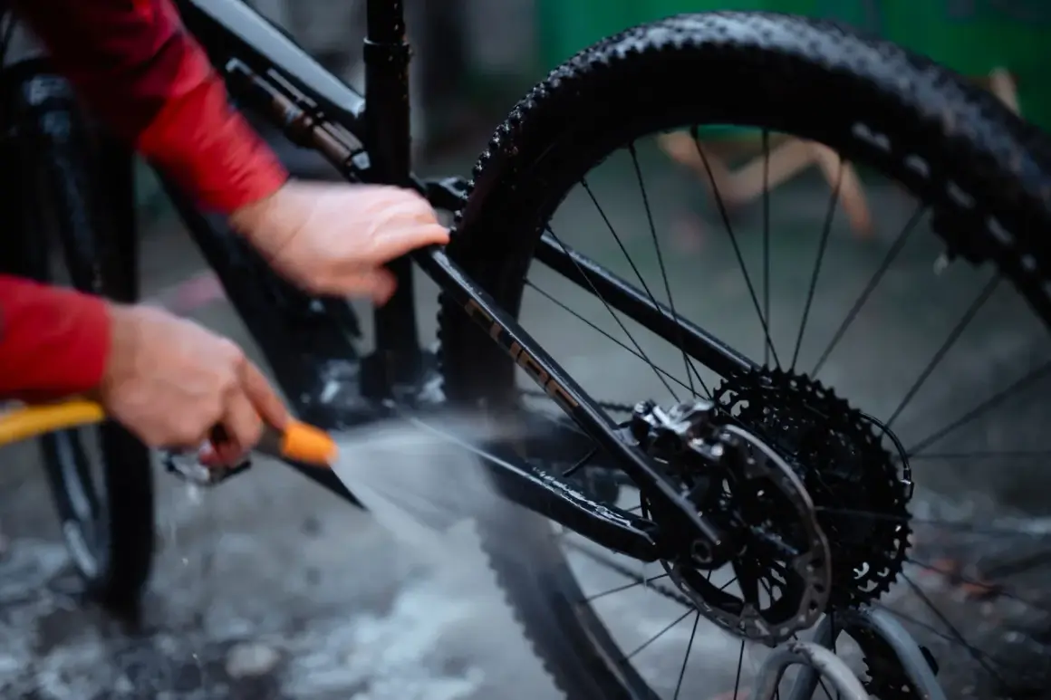 Iemand maakt de fietsketting schoon met Dasty, terwijl de rest van de fiets nat wordt gespoten.