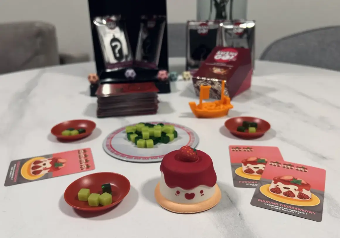 Gra Sushi Go Party! z uroczym puddingiem truskawkowym i kostkami do gry.