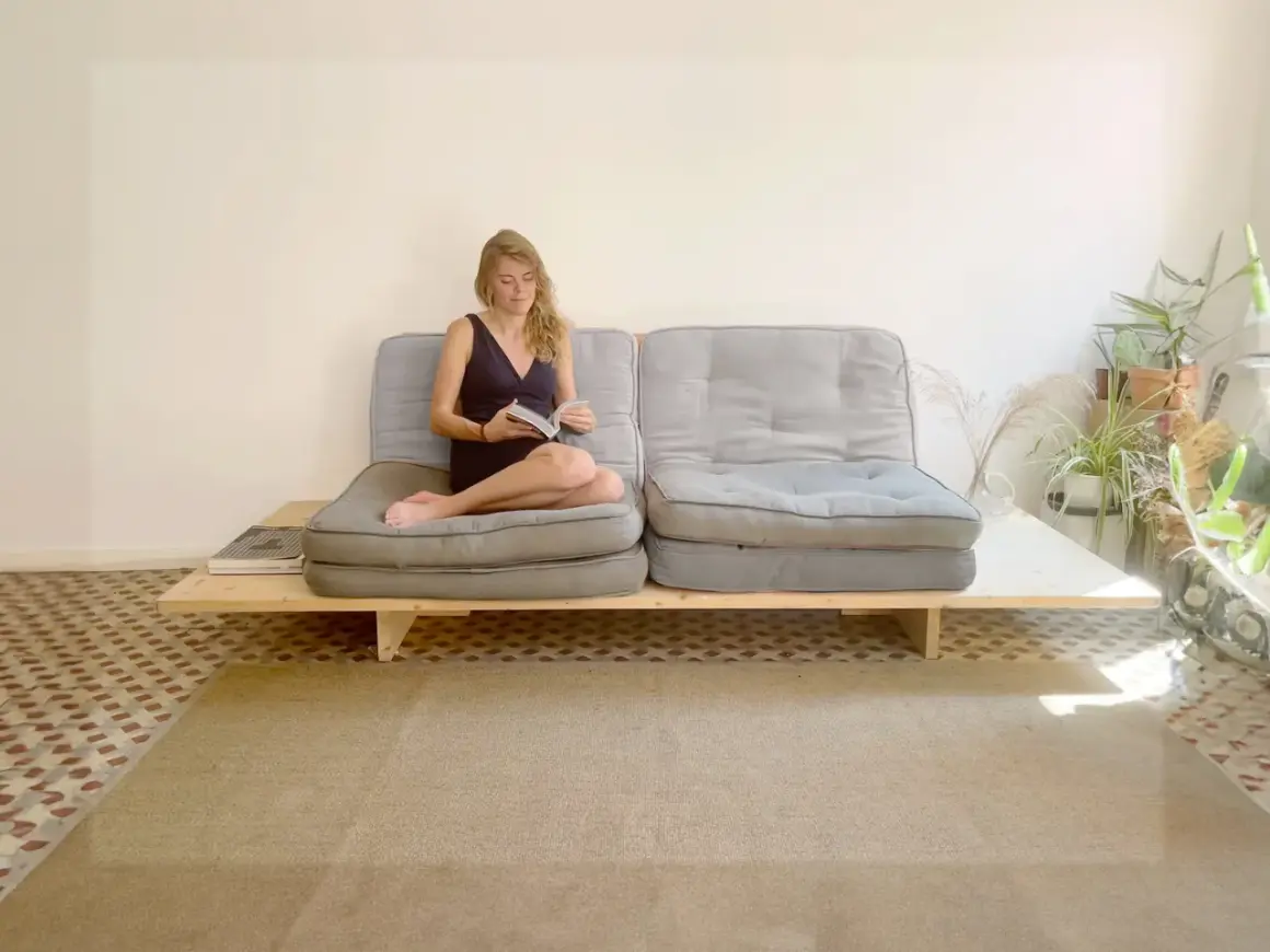 Frau liest auf einem selbstgebauten Sofabett mit grauen Polstern und Holzrahmen.