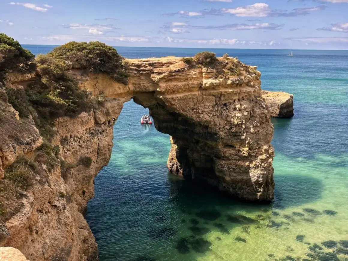 Arco natural de roca en el mar turquesa, ideal para tu plan de qué ver en Algarve en 5 días. Un bote turístico pasa por debajo.