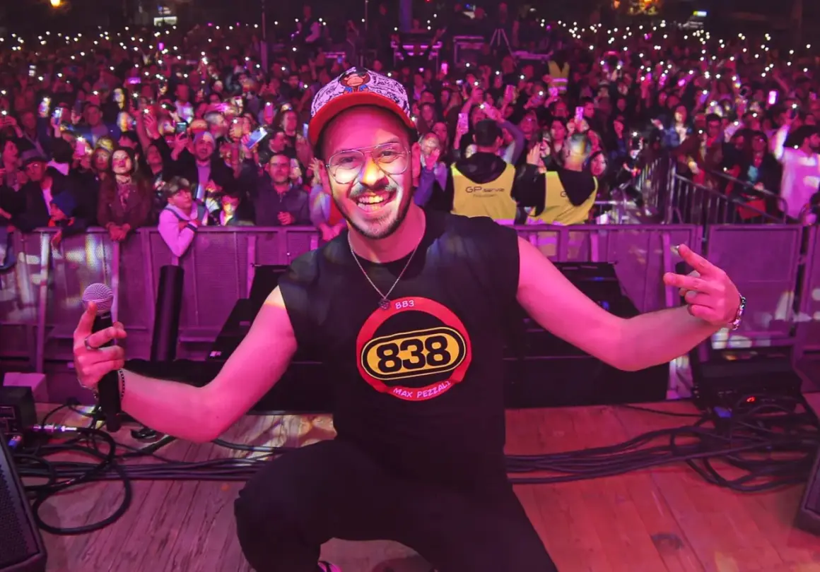 Max Pezzali sul palco, con la folla illuminata dai cellulari, indossa una maglietta con il logo 883.