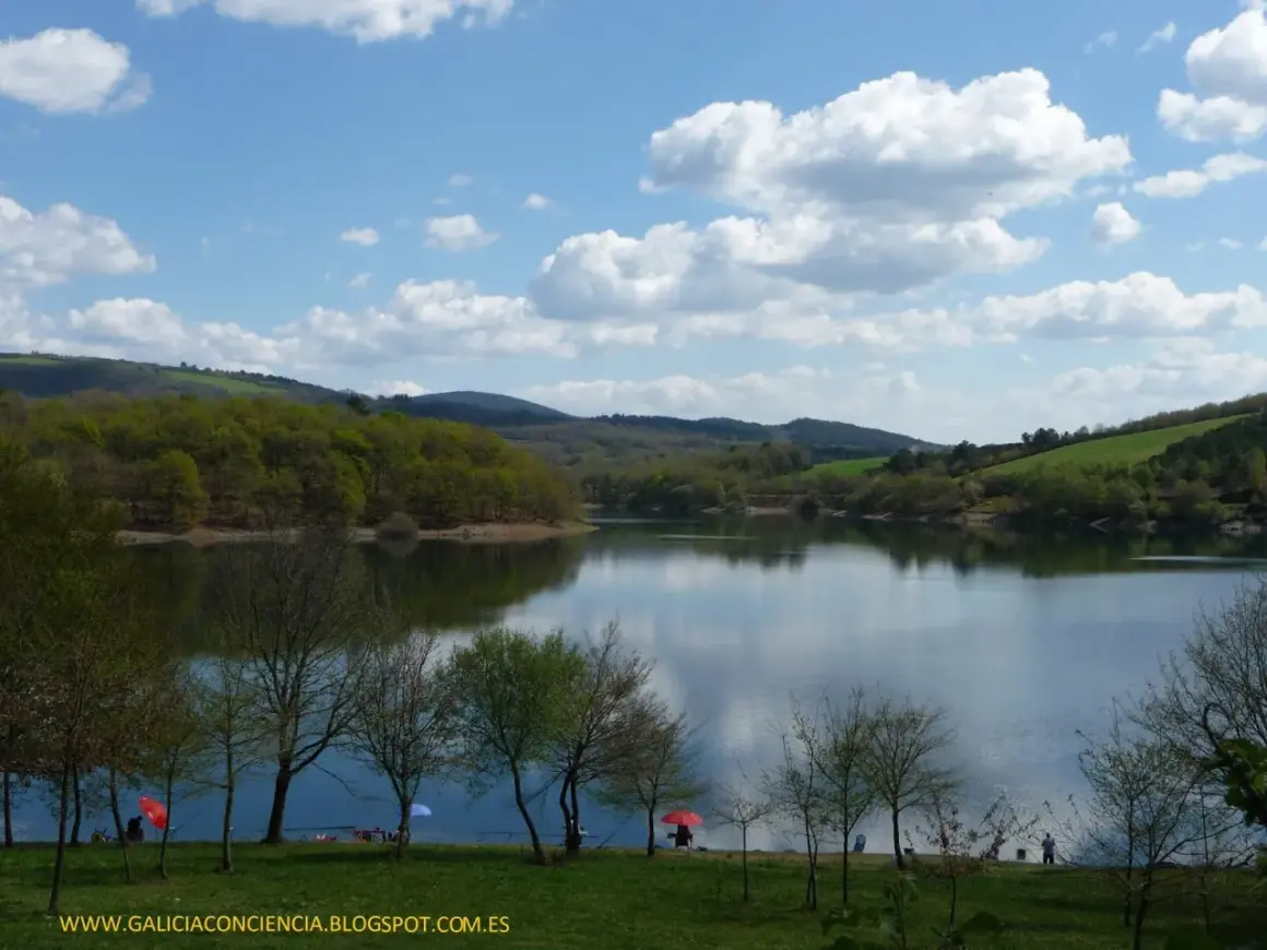 El embalse de Vilasouto, con sus aguas serenas reflejando el cielo azul y las verdes colinas, invita a disfrutar de un día tranquilo.