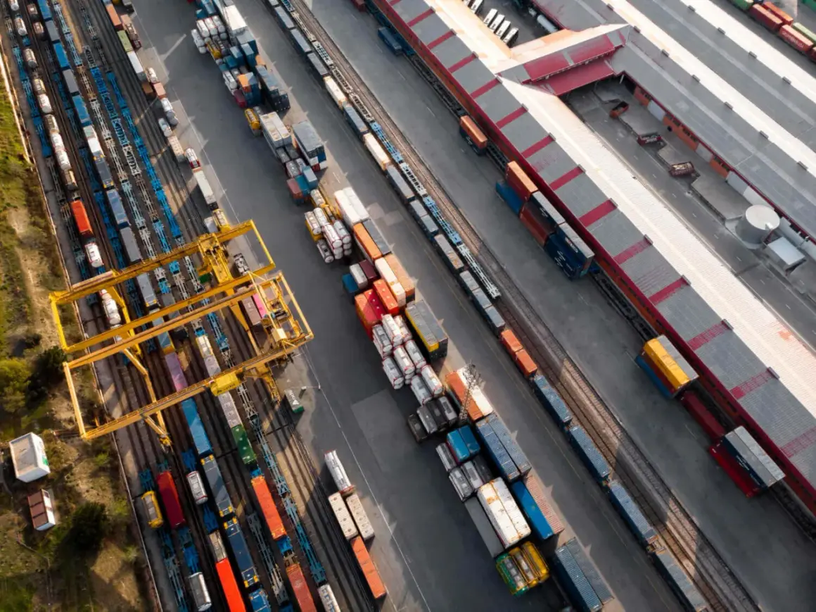 Widok z lotu ptaka na terminal kolejowy, gdzie odbywa się transport intermodalny. Żurawie przeładowują kontenery między pociągami a ciężarówkami.