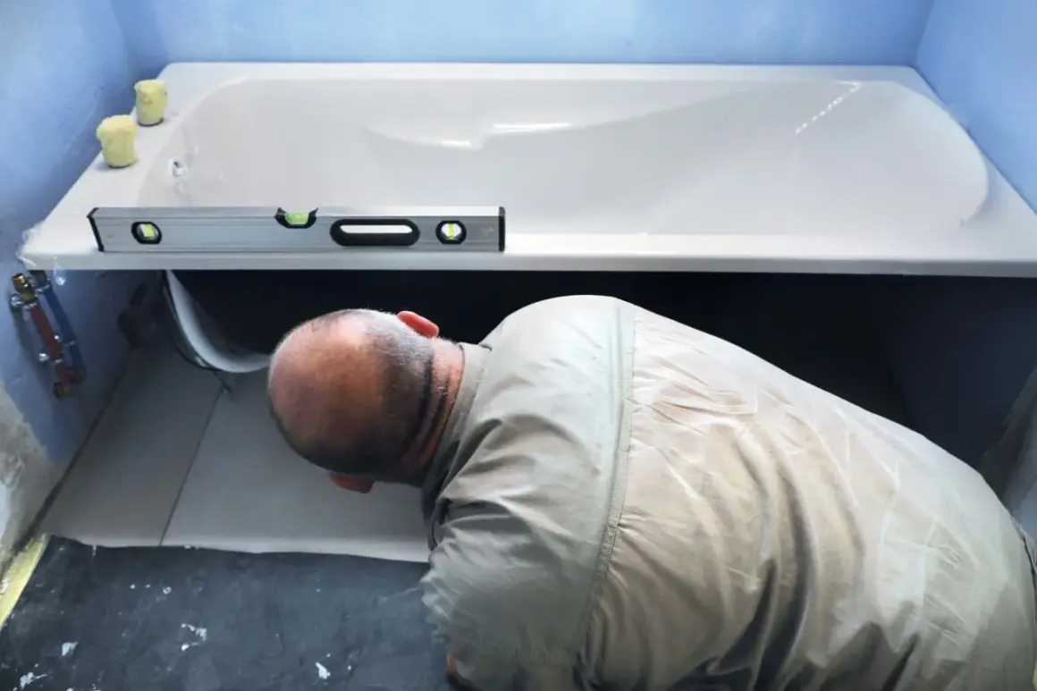 Un homme vérifie le niveau d'une baignoire avant de la fixer. L'outil de mesure est posé sur le rebord.