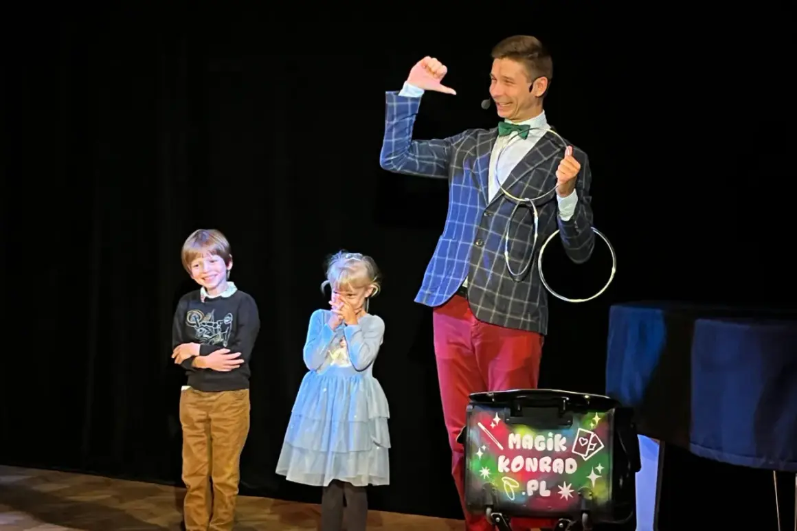 Magik Konrad wyjaśnia dzieciom, co to jest teatr, podczas pokazu iluzji. Dzieci z zaciekawieniem obserwują sztuczki.