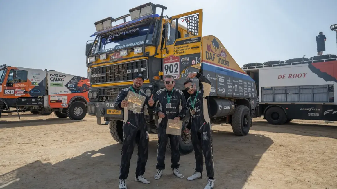 Trzej członkowie zespołu KAMENA Rally Team pozują z pucharami przed ciężarówką DAF.