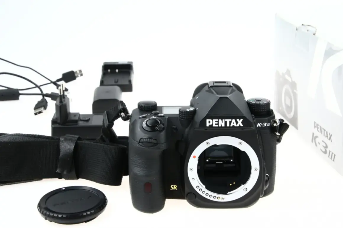 Czarny aparat Pentax K-3 III, ładowarka i akcesoria. Czy to lustrzanka czy bezlusterkowiec? To lustrzanka.