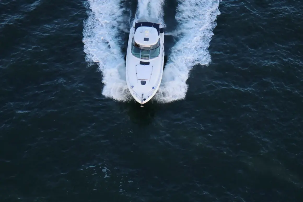 Un bianco yacht naviga veloce, lasciando una scia di spuma. La sua posizione è centrale, in un mare scuro e mosso.