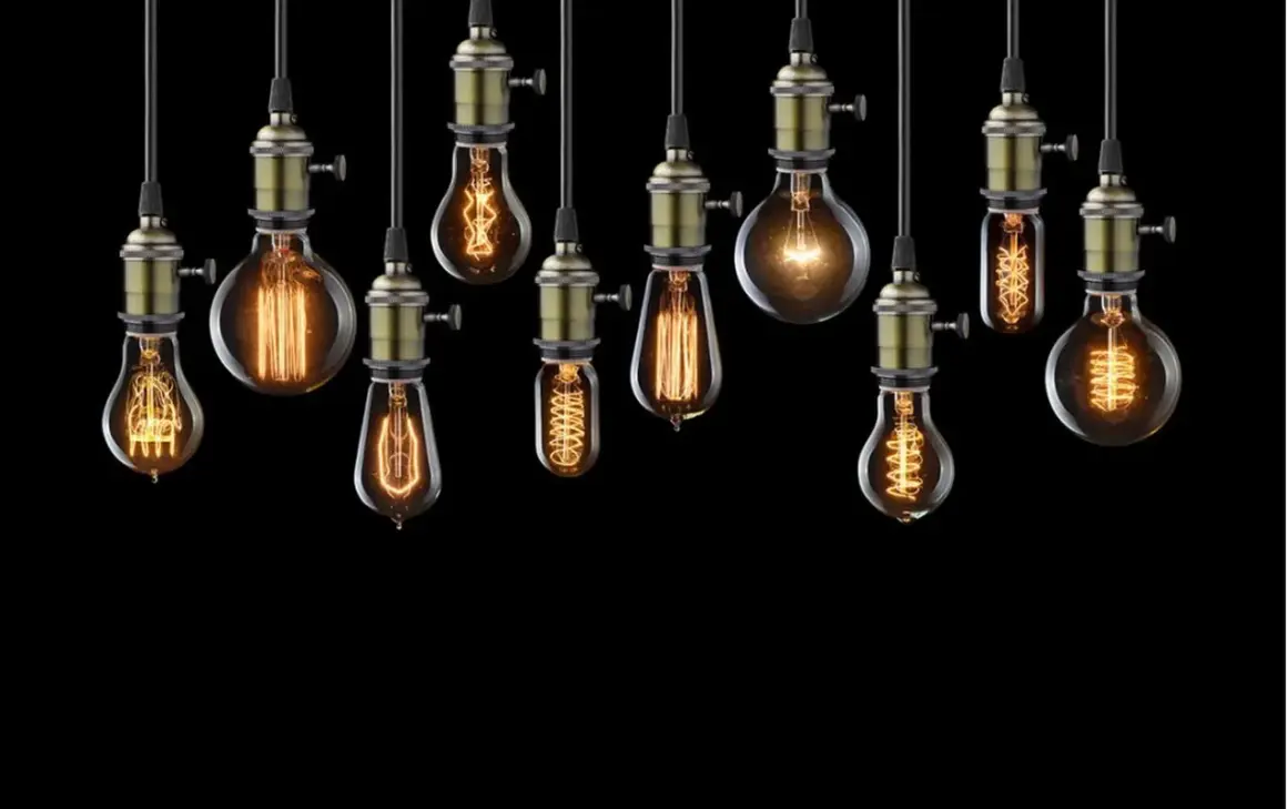 Rząd wiszących lamp w kształcie żarówki, każda z unikalnym, ozdobnym żarnikiem i mosiężnym mocowaniem, tworzy ciepłą, nostalgiczną atmosferę.