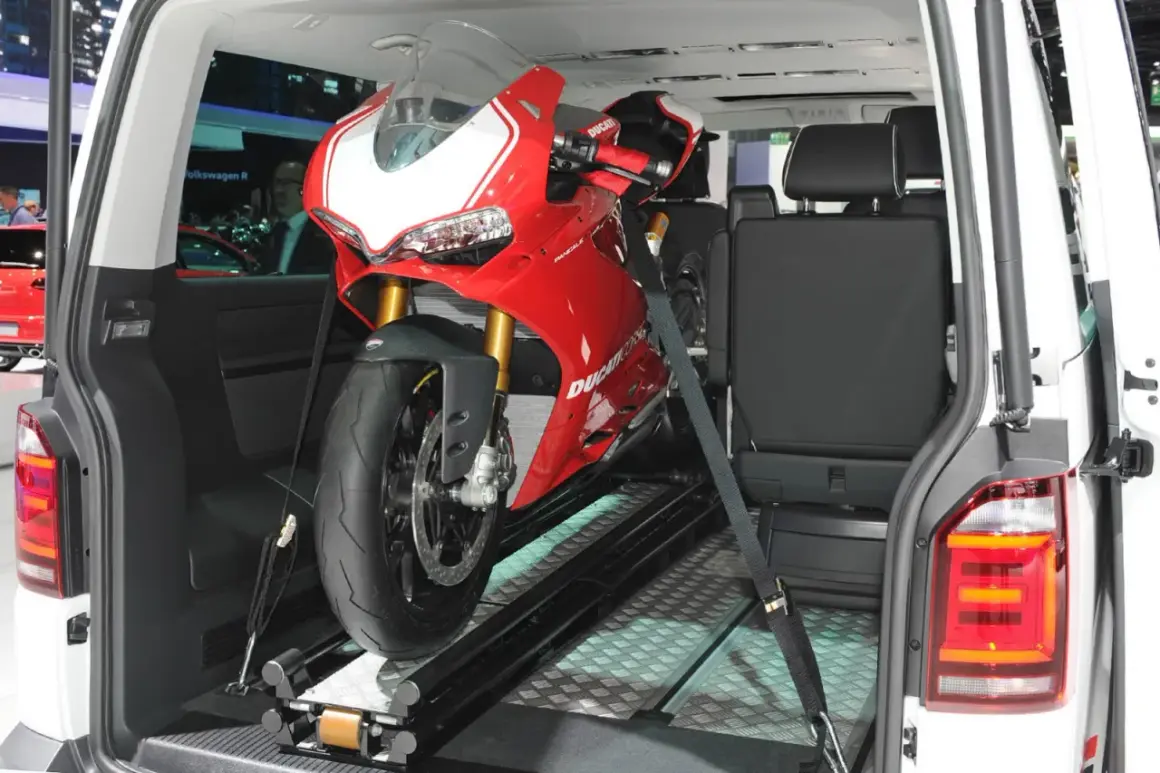 Una moto deportiva roja lista para transportar en furgoneta, asegurada con correas sobre un riel.