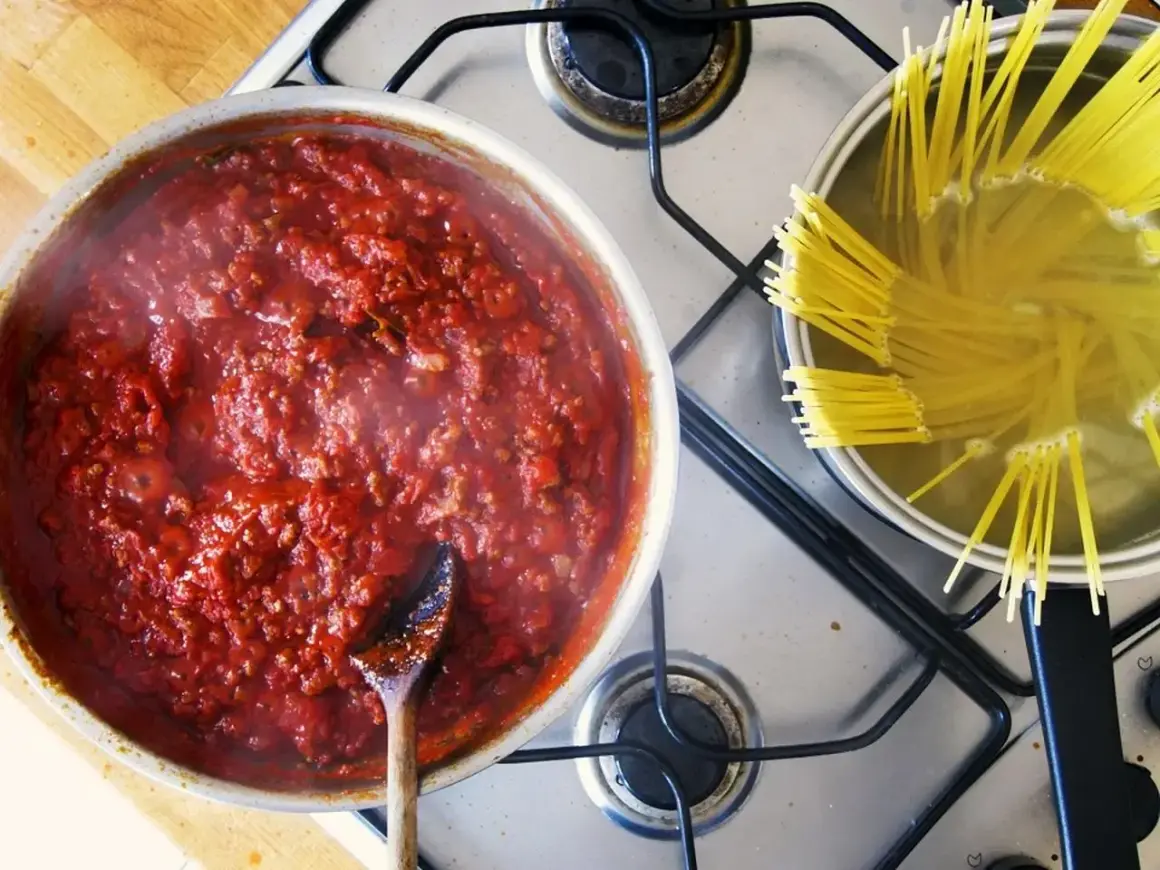 Gotowy do podania, aromatyczny sos do spaghetti gotuje się obok makaronu w garnku.