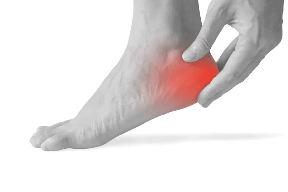 Mano che preme sul tallone sinistro, evidenziato in rosso, per indicare dolore al tallone sinistro a riposo.