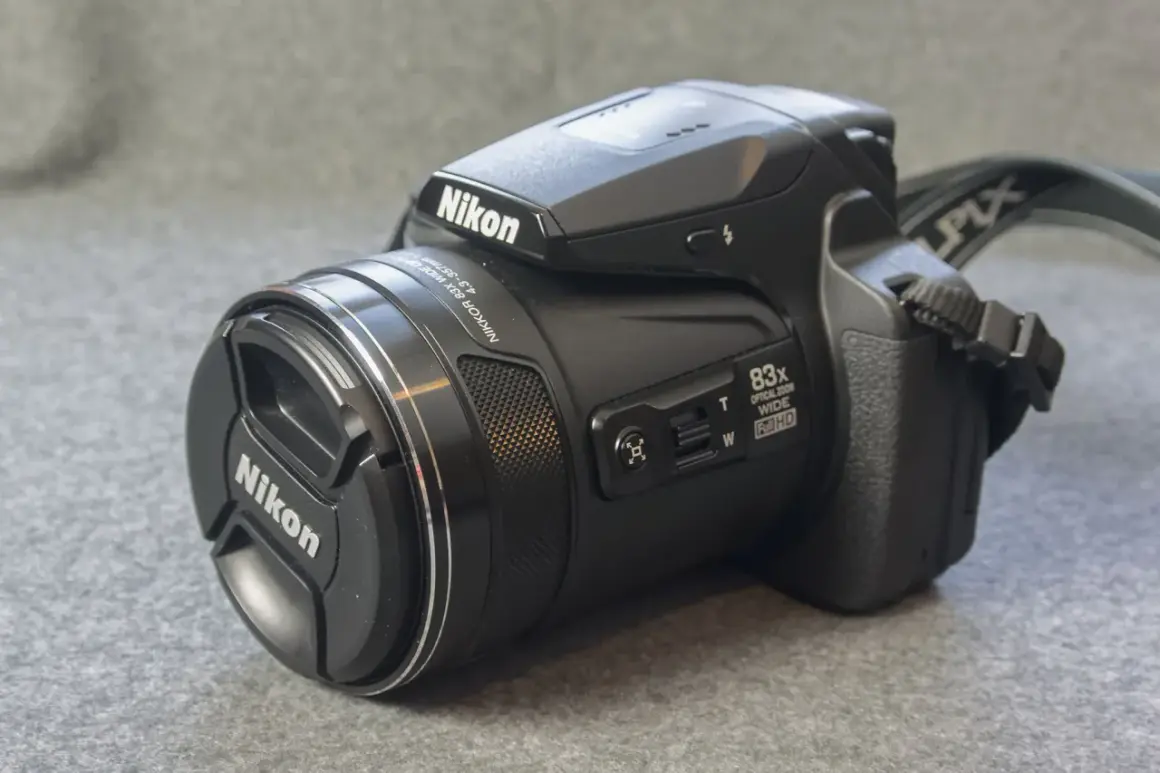 A black Nikon P90 camera with an 83x optical zoom lens sits on a textured gray surface.