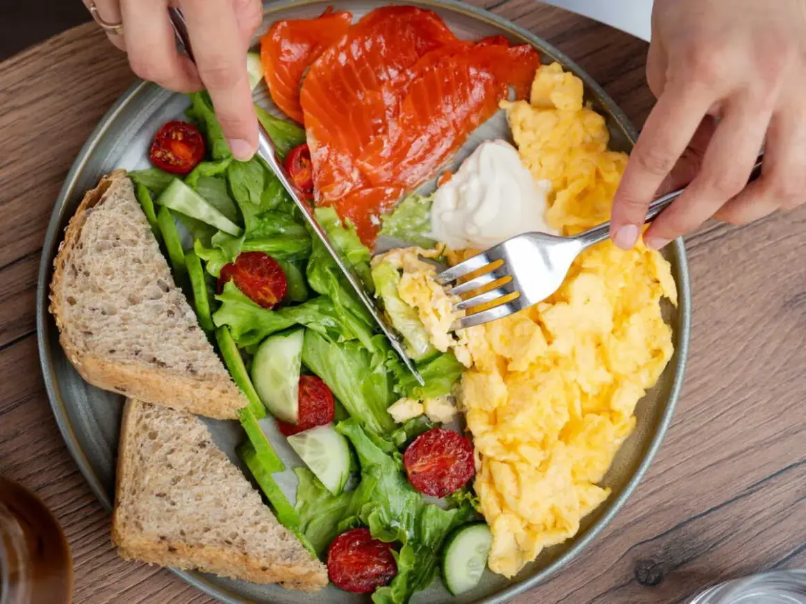 Assiette colorée avec saumon fumé, œufs brouillés, salade verte, tomates séchées, concombre et pain complet. Un repas protéiné parfait pour bien commencer la journée.