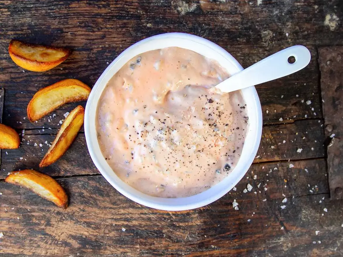 En skål med krämig hamburgerdressing, perfekt för ditt nästa hamburgerdressing recept. Serveras med klyftpotatis på en träbakgrund.