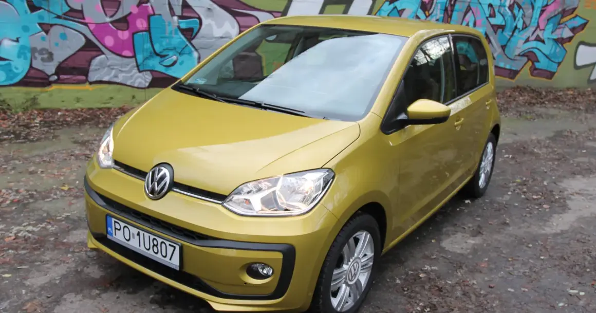 Żółty Volkswagen up! zaparkowany pod kolorowym graffiti.