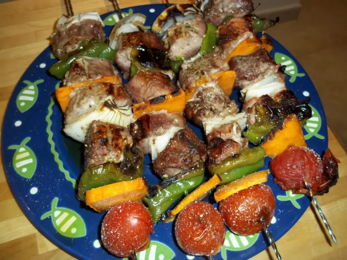 Brochetas de solomillo con pimientos verdes, cebolla y tomate, servidas en un plato azul con dibujos de peces.