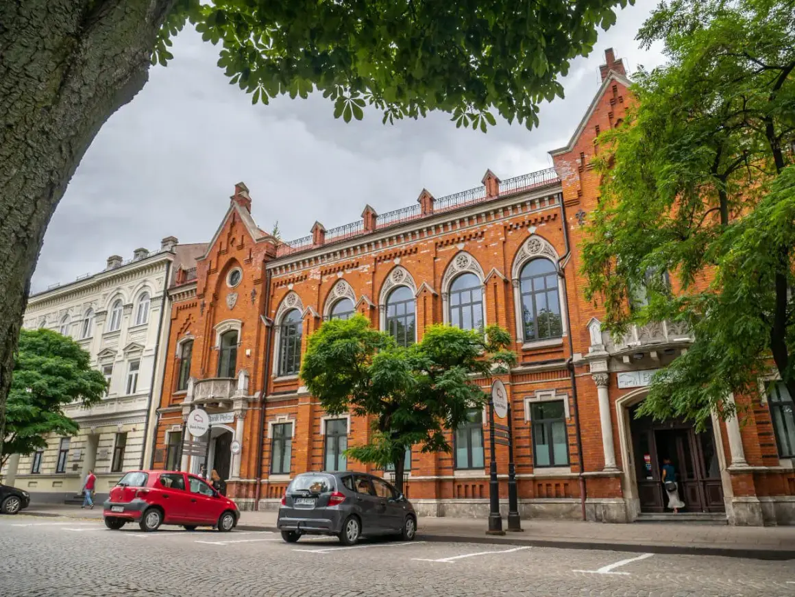 Kamienice w Radomiu, w tym Bank Polski, to ciekawe atrakcje miasta. Dwa samochody zaparkowane na brukowanej ulicy.