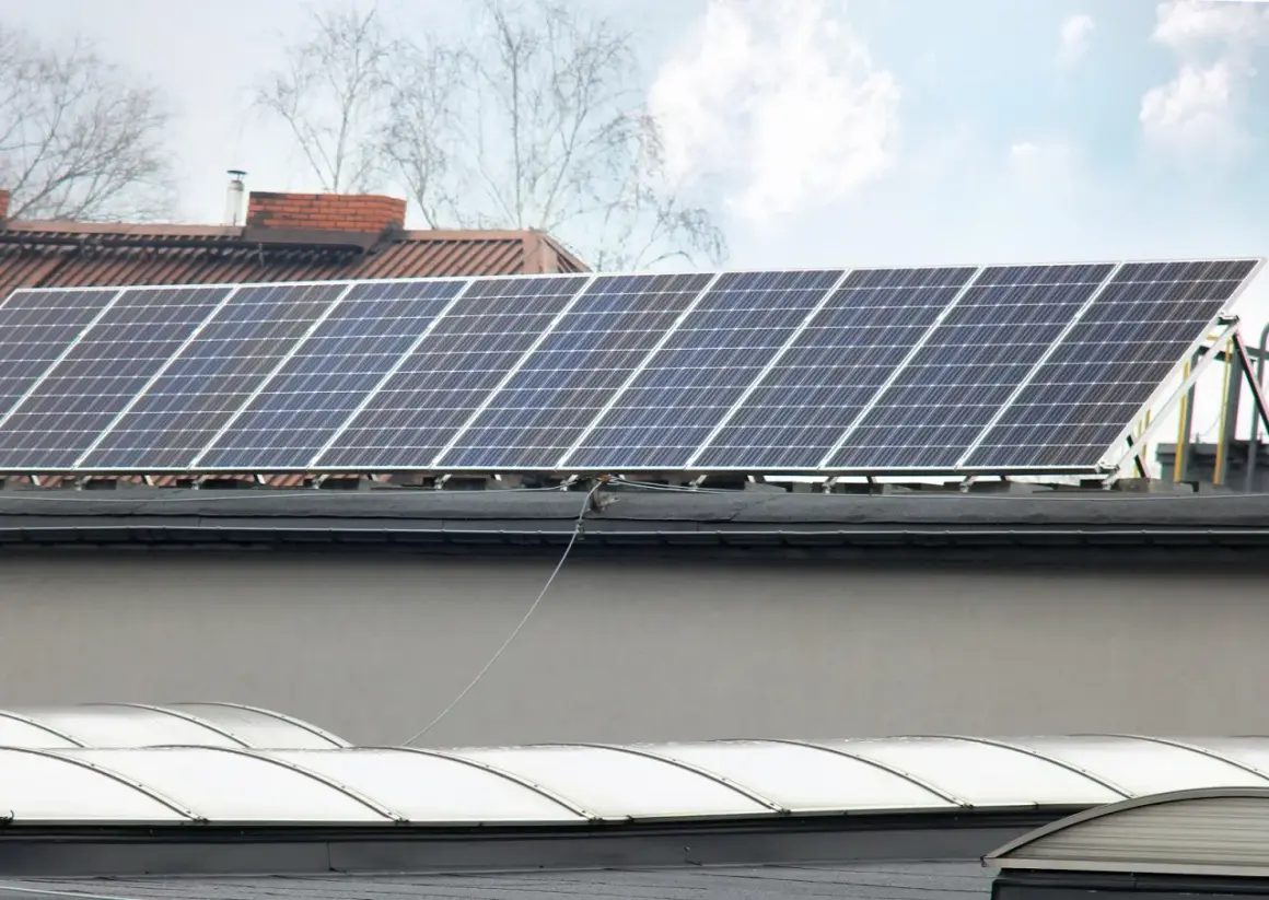 Panele fotowoltaiczne na dachu, gotowe do podgrzewania i produkcji energii. W tle budynki i drzewa.