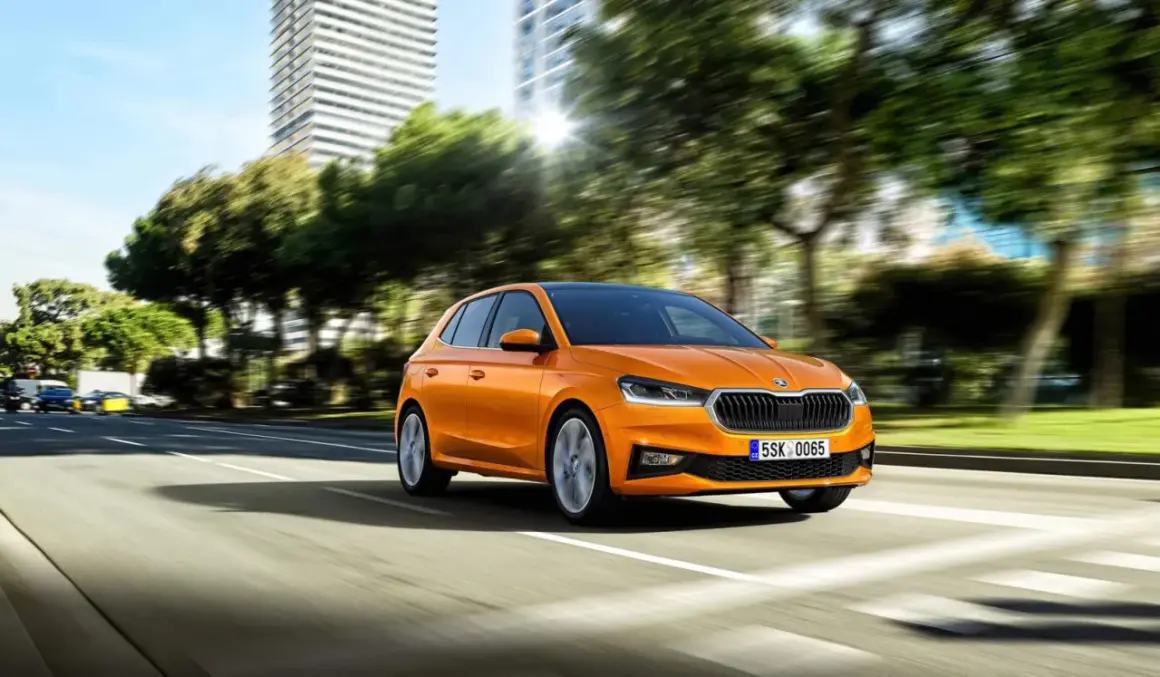 Pomarańczowa Skoda Fabia jedzie po mieście. Idealny samochód, by nauczyć się, co trzeba umieć na pierwszą jazdę.