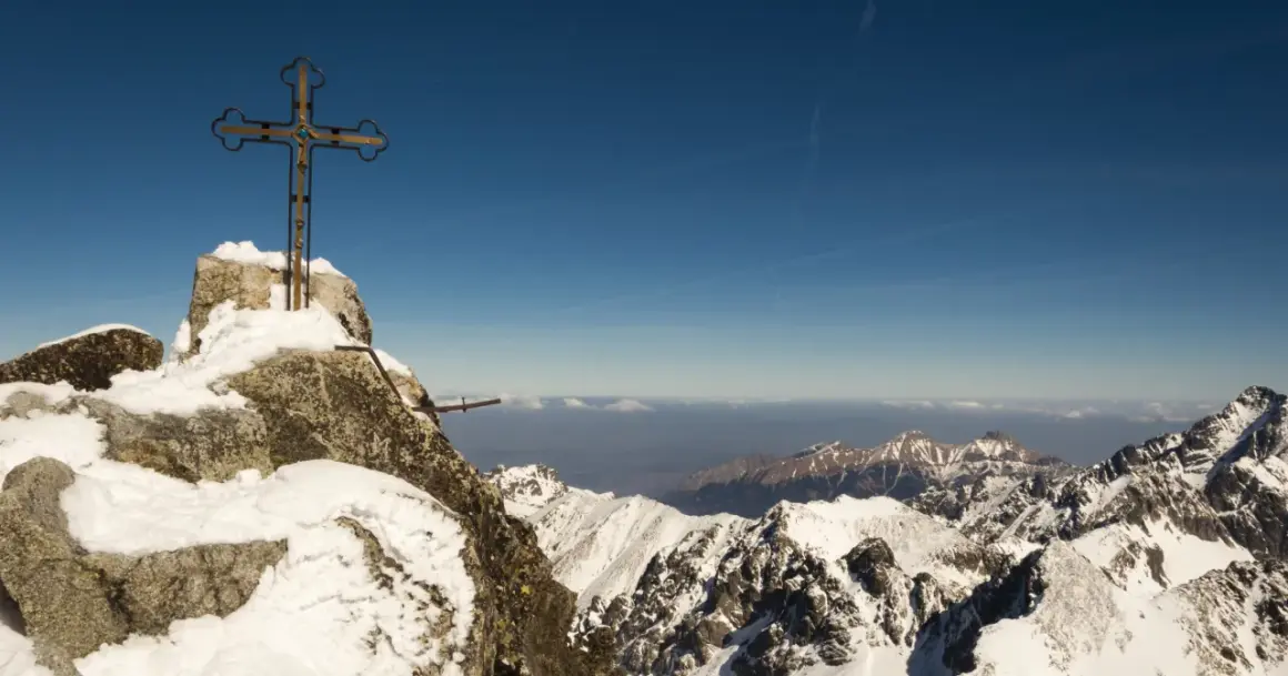 Szczyt Gerlach bez przewodnika. Krzyż na skalistym, ośnieżonym wierzchołku, w tle zimowe Tatry i błękitne niebo.